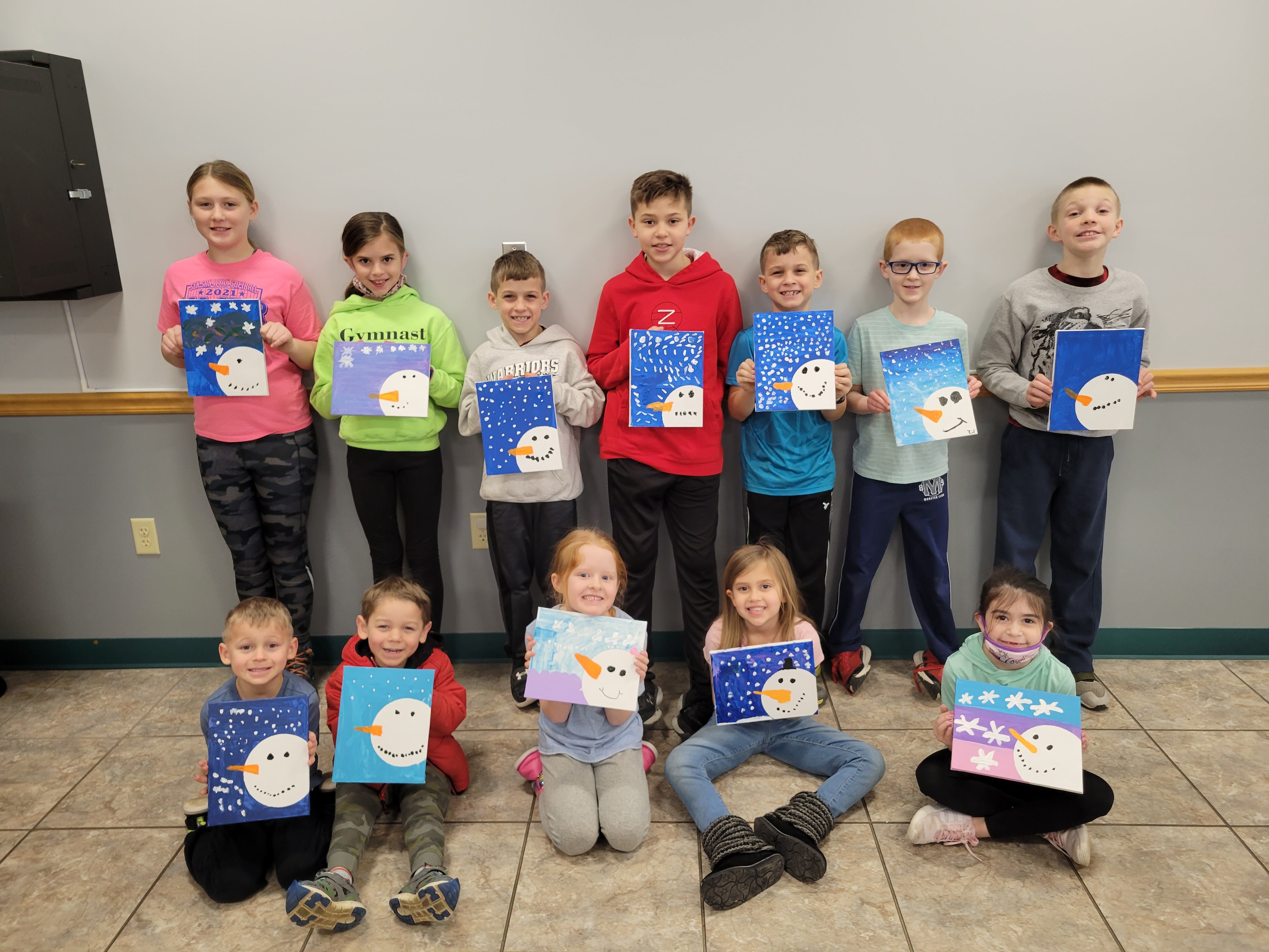 Group picture of children at the library, each holding a snowman painting